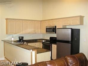 Kitchen with stainless steel appliances, dark countertops, a peninsula, and light brown cabinetry