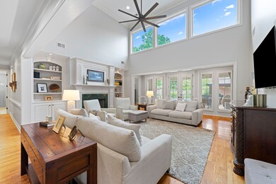 The expansive great room features a two-story ceiling, abundant natural light from large windows, a cozy gas fireplace, and built-in bookshelves, creating a warm and welcoming atmosphere.
