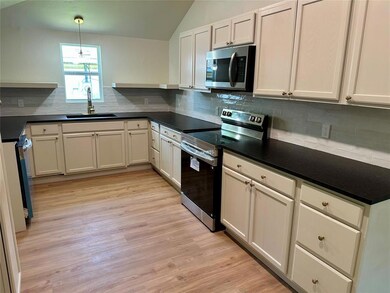 Kitchen featuring stainless steel appliances, a sink, decorative backsplash, dark countertops, and light wood-style floors