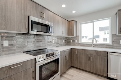 Kitchen featuring stainless steel appliances, backsplash, recessed lighting, light wood-style flooring, and light stone countertops