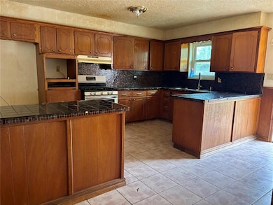 Kitchen featuring brown cabinets, a peninsula, decorative backsplash, stainless steel gas range, and a textured ceiling