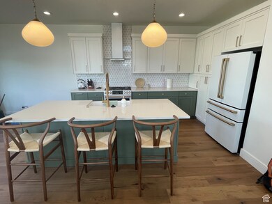 Kitchen with high end white refrigerator, dark wood-type flooring, wall chimney exhaust hood, backsplash, and light countertops