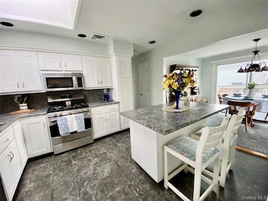 Kitchen featuring appliances with stainless steel finishes, white cabinetry, a breakfast bar area, tasteful backsplash, and recessed lighting
