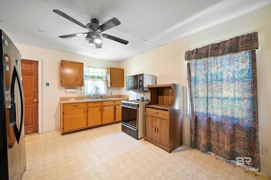 Kitchen with light flooring, freestanding refrigerator, gas range, light countertops, and a ceiling fan