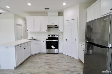 Kitchen with stainless steel appliances, a peninsula, light countertops, white cabinets, and recessed lighting