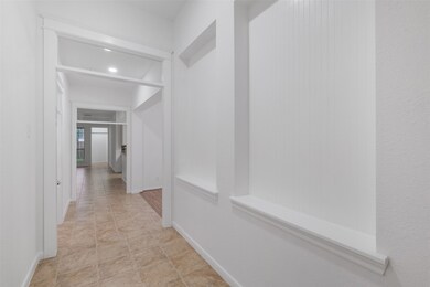 There is a bright and airy corridor featuring tiled flooring, neutral color walls, and white trim, leading to a well-lit Home Office with a view of the outdoors through French glass doors. The passage includes architectural details like a recessed niche, perfect for decorative elements or storage.