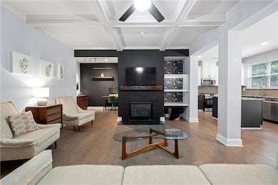 Living room featuring hardwood / wood-style flooring, a fireplace with flush hearth, coffered ceiling, beamed ceiling, and crown molding