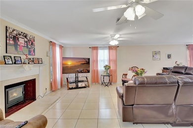 Living room with a glass covered fireplace, ceiling fan, light tile patterned flooring, and crown molding