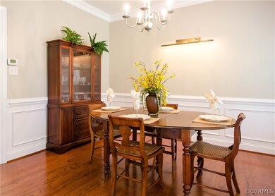The dining room has hardwood flooring, double crown molding, chair rail and decorative picture frame molding, silver chandelier, wall light for art display, and is open to the foyer and kitchen.