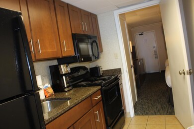 Kitchen featuring black appliances, brown cabinetry, dark stone counters, light tile patterned floors, and light carpet
