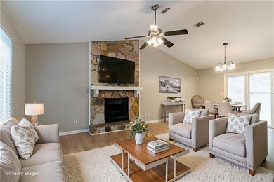 Living area featuring wood finished floors, ceiling fan, a fireplace, a chandelier, and baseboards