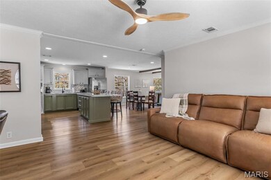 Living room with light wood-style flooring, ceiling fan, ornamental molding, and recessed lighting