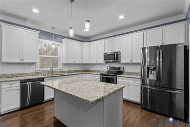 Kitchen with appliances with stainless steel finishes, white cabinetry, a kitchen island, crown molding, and dark wood-style flooring