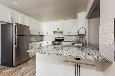 Kitchen with appliances with stainless steel finishes, a peninsula, stone counters, backsplash, and white cabinetry