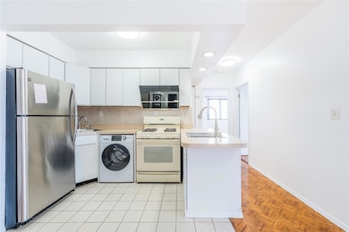 Kitchen featuring freestanding refrigerator, gas range gas stove, washer / clothes dryer, a peninsula, and white cabinets