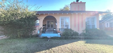View of exterior entry featuring a chimney, a lawn, roof with shingles, and covered porch