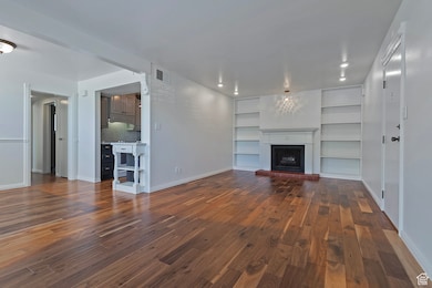 Unfurnished living room with built in features, a brick fireplace, and dark wood finished floors