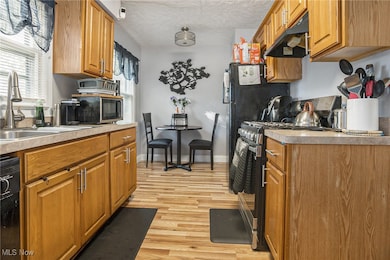 Kitchen with appliances with stainless steel finishes, under cabinet range hood, light wood-style flooring, brown cabinetry, and a textured ceiling