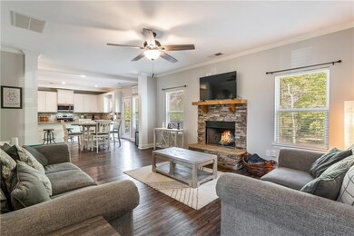 Living room featuring ornamental molding, dark wood-style floors, a stone fireplace, and a ceiling fan