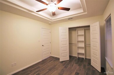 Unfurnished bedroom featuring a tray ceiling, dark wood-type flooring, a closet, baseboards, and a ceiling fan