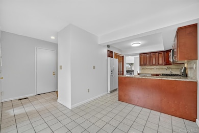 Kitchen featuring light stone counters, white fridge with ice dispenser, a peninsula, tasteful backsplash, and light tile patterned floors