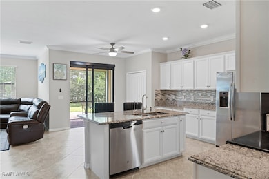 Kitchen featuring crown molding, white cabinets, appliances with stainless steel finishes, decorative backsplash, and light stone countertops