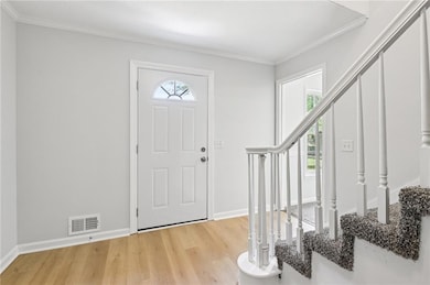 Foyer entrance featuring stairs, light wood-style floors, ornamental molding, and baseboards