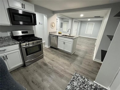 Kitchen featuring stainless steel appliances, wood finished floors, a sink, light stone countertops, and baseboards