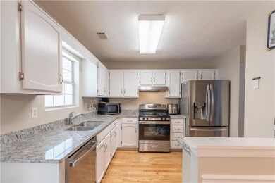 Kitchen with stainless steel appliances, under cabinet range hood, light wood-type flooring, white cabinetry, and a textured ceiling