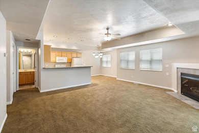 Open Living Area featuring carpet floors, a tiled fireplace, a chandelier, ceiling fan, and a raised ceiling