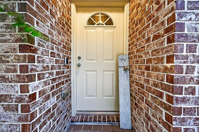 Inviting entryway featuring a cream-colored door with a semi-circular window, surrounded by charming red brick walls. A welcoming sign adds a personal touch.
