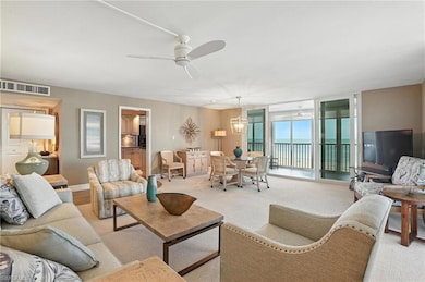 Living room featuring light colored carpet, ceiling fan, and a wall of windows - Virtually Edited Image