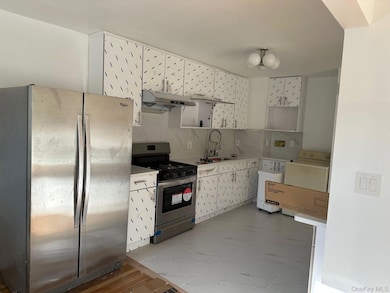 Kitchen featuring appliances with stainless steel finishes, tasteful backsplash, white cabinetry, light countertops, and under cabinet range hood