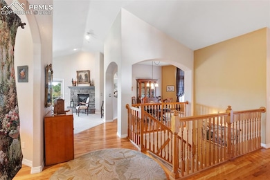 Corridor with an upstairs landing, lofted ceiling, wood finished floors, arched walkways, and a chandelier