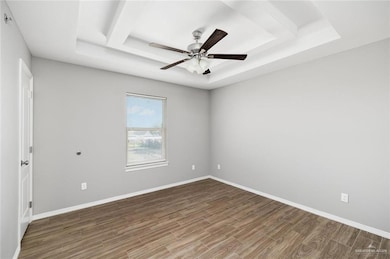 Spare room featuring a tray ceiling, wood finished floors, and ceiling fan