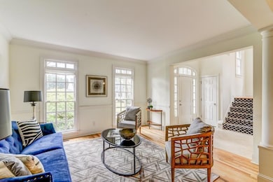 Living room with ornamental molding, decorative columns, light wood-style floors, wainscoting, and stairway