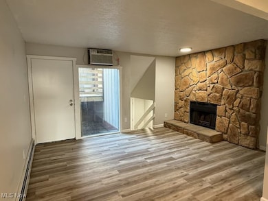 Unfurnished living room with baseboard heating, a textured ceiling, wood finished floors, a fireplace, and an AC wall unit
