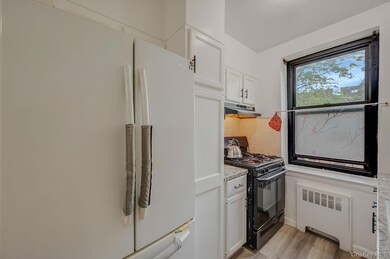 Kitchen featuring freestanding refrigerator, gas stove, radiator heating unit, white cabinetry, and light wood finished floors