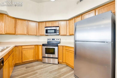 Kitchen featuring appliances with stainless steel finishes, light countertops, light wood-type flooring, and light brown cabinetry