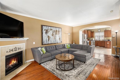 Living area with arched walkways, light wood finished floors, ornamental molding, and a fireplace