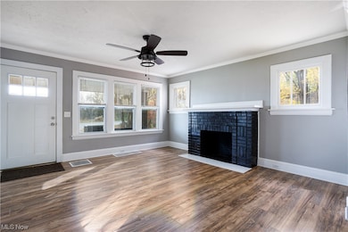 Unfurnished living room with dark hardwood / wood-style flooring, ceiling fan, a brick fireplace, and crown molding