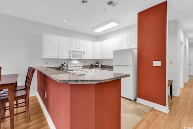 Kitchen featuring white appliances, a peninsula, white cabinets, and light wood-style floors