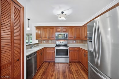 Kitchen featuring stainless steel appliances, brown cabinetry, decorative backsplash, dark wood finished floors, and hanging light fixtures