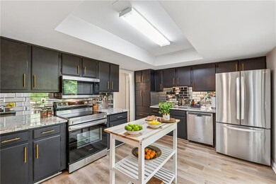 Kitchen with appliances with stainless steel finishes, a raised ceiling, tasteful backsplash, light wood finished floors, and light stone countertops