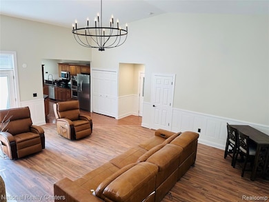 Living room with wainscoting, a decorative wall, wood finished floors, high vaulted ceiling, and a chandelier