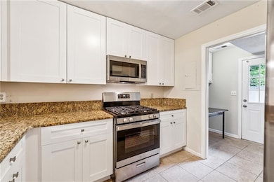 Kitchen with appliances with stainless steel finishes, white cabinets, light tile patterned flooring, and light stone counters