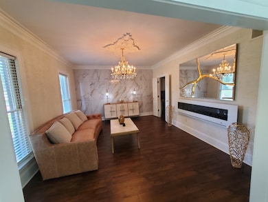 Living room featuring a chandelier, ornamental molding, wood finished floors, and baseboards