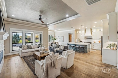 Living room with a ceiling fan, light wood-style floors, a textured ceiling, a raised ceiling, and recessed lighting