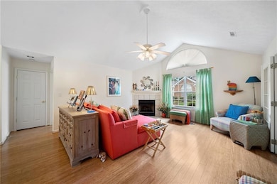 Living area with lofted ceiling, wood finished floors, a fireplace, and a ceiling fan