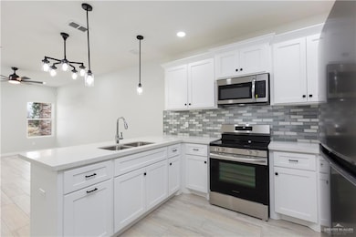 Kitchen with hanging light fixtures, ceiling fan, sink, stainless steel appliances, and kitchen peninsula